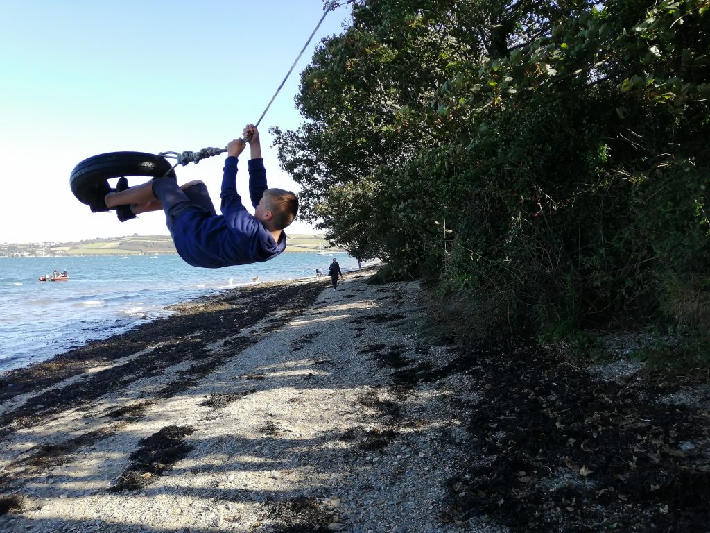 boy swinging on tyre by river feeling confident