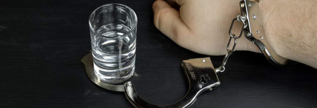 hand which is handcuffed to a glass of gin